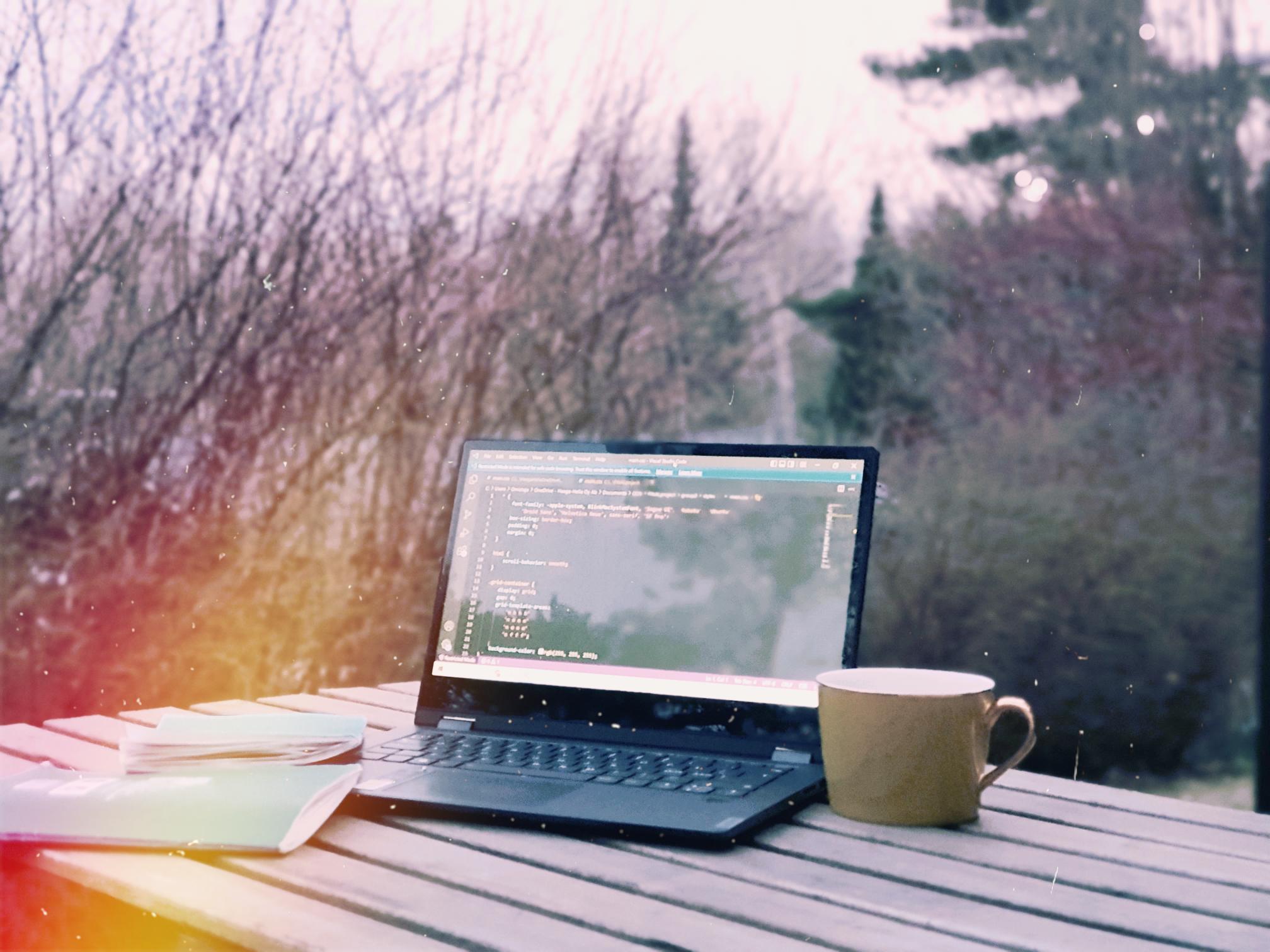 Laptop on a table next to a mug and a notebook